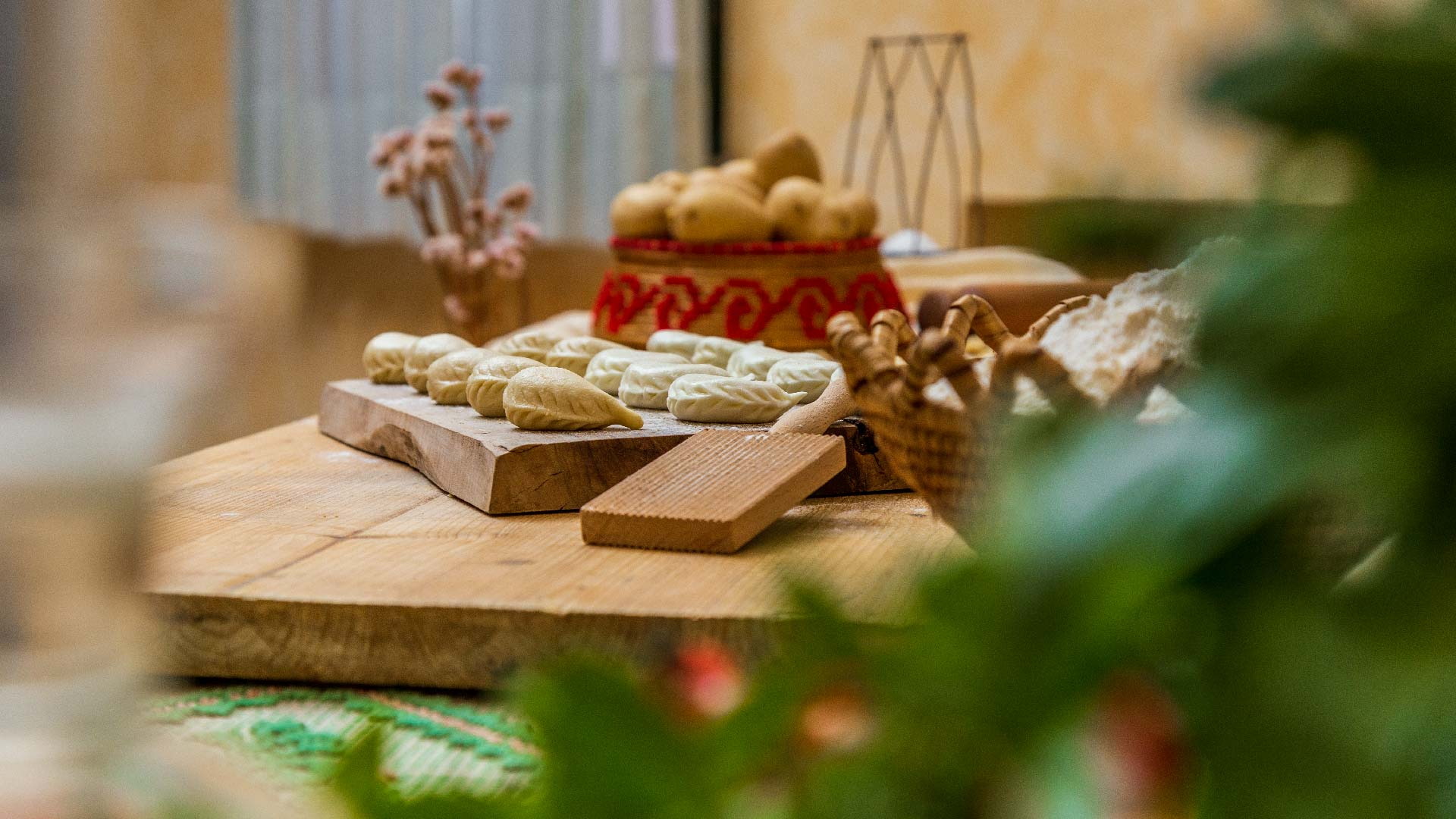 Freshly hand-sealed culurgiones on a wooden board next to flour and a traditional basket